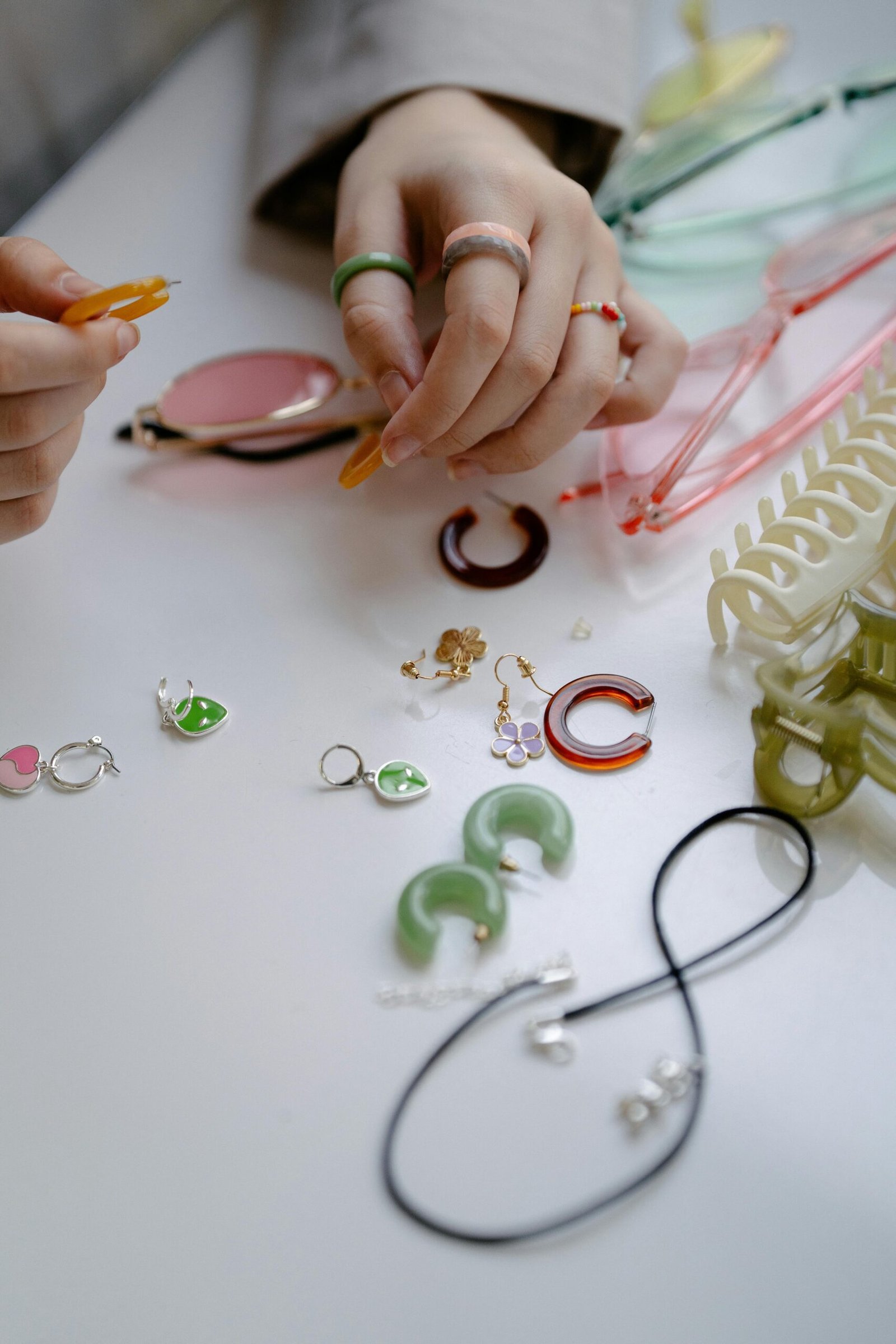 Hands arranging colorful jewelry and accessories on a white surface, ideal for craft enthusiasts.